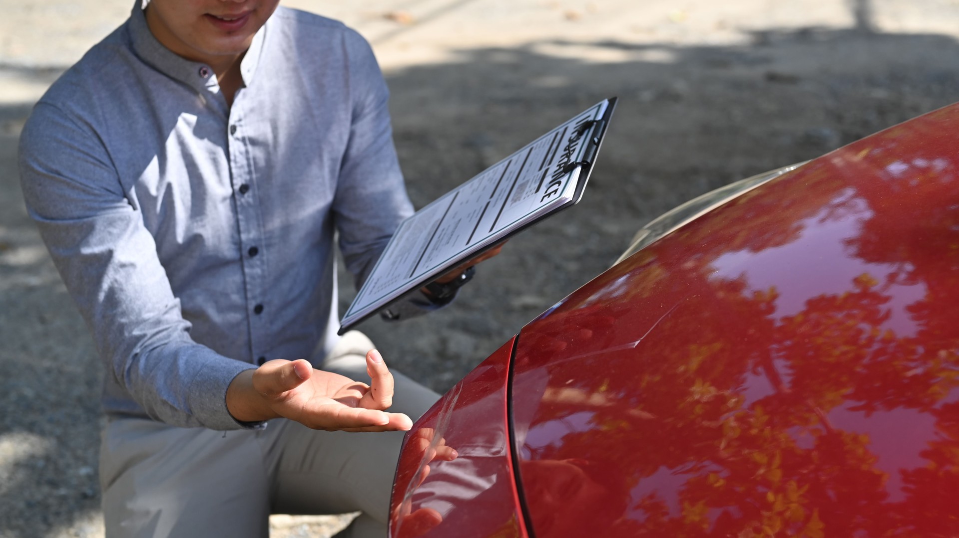 Cropped shot male insurance agent holding claim form and inspecting damaged car.